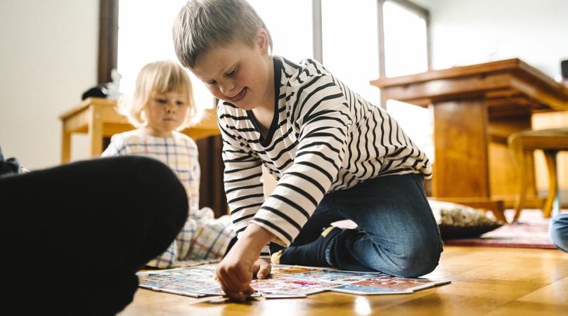 Pojke lägger pussel och en yngre flicka kollar på. 