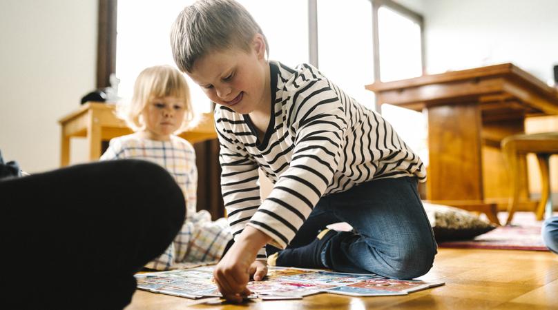 Boy with disability solving jigsaw puzzle sitting by father and sister in living room at home