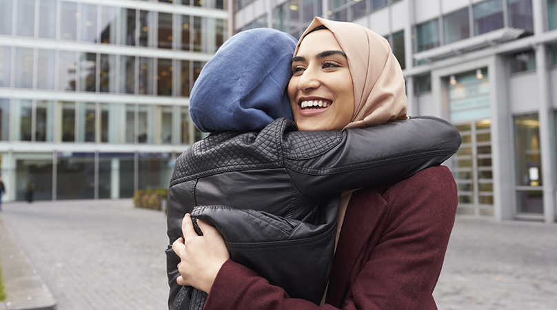 Två personer kramas. Ena personen ser snett förbi kameran medan andra är vänd bort. Båda människorna bär slöja.