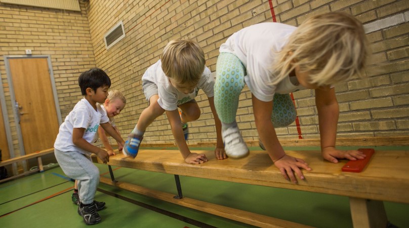 Fyra barn i 3-4 års ålder klättrar på en gymnastikbänk.