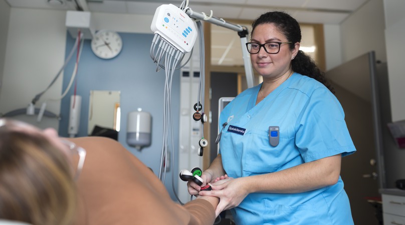 Sjuksköterska sätter ekg på en patient som ligger på en brits.