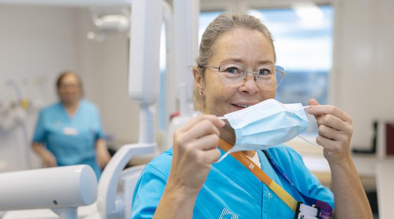 En kvinna håller ett munskydd framför ansiktet, bakom henne syns en tandläkarstol.
