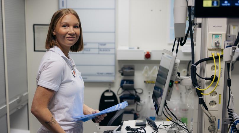 En kvinna i vårdkläder står framför en dator och håller i en präm.