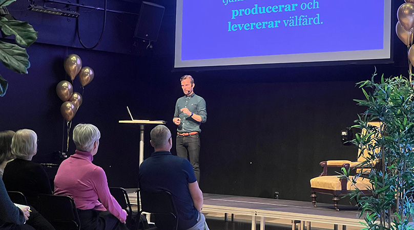En man (Morten Hyllegaard) står framme på en scen och framför honom sitter en publik.