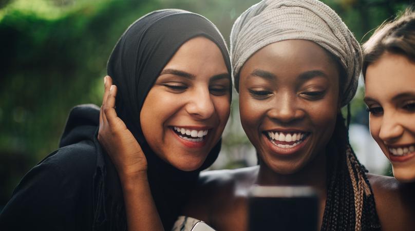 Smiling multi-ethnic friends looking at mobile phone while standing in backyard