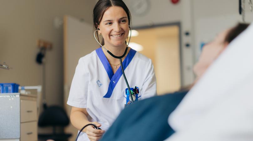 En kvinna i vårdkläder tar blodtrycket på en patient i sjukhussäng.