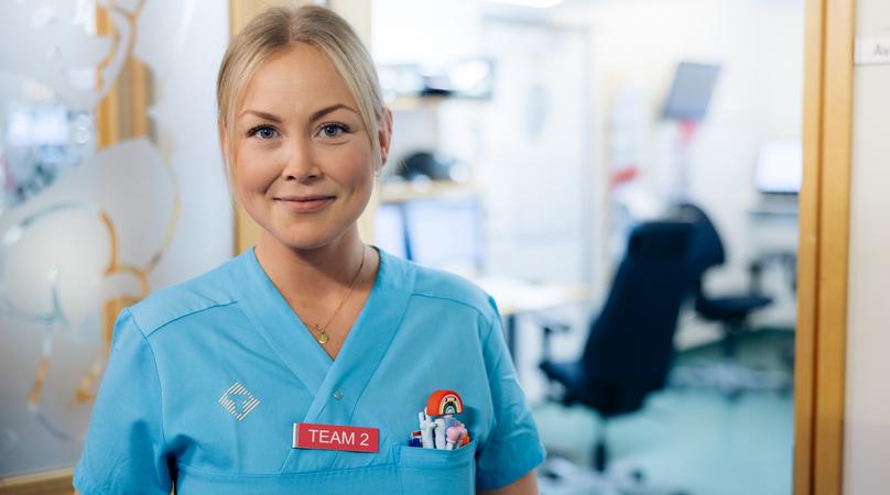 En kvinna i vårdkläder står i en dörröppning.