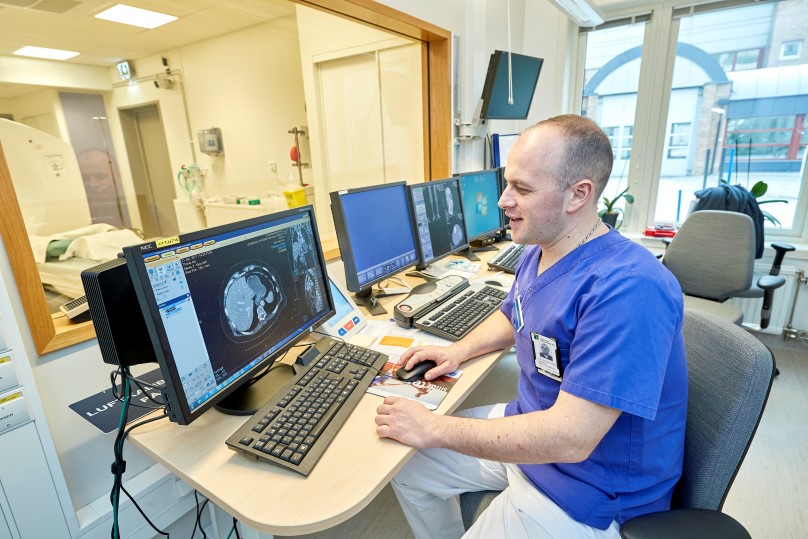 En röntgensjuksköterska sitter och kollar på röntgenbilder på dataskärmar.