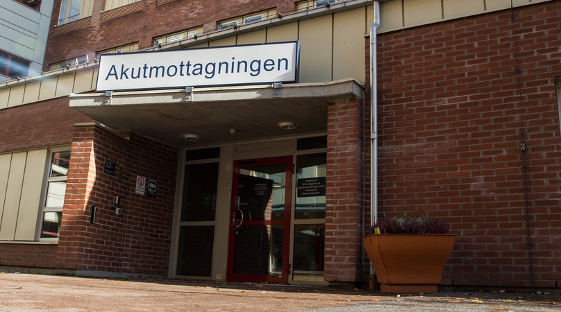 Ingång till brun tegelbyggnad. Över dörren hänger en skylt där det står Akutmottagningen.