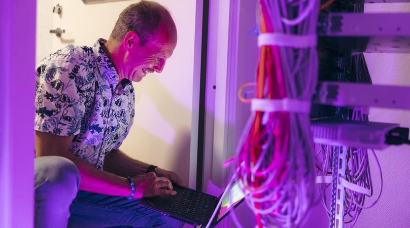 Man jobbar med dator i ett skåp med nätverkssladdar.