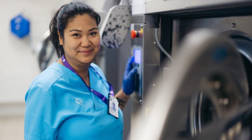 En kvinna som jobbar i lokalvården står intill en stor tvättmaskin.