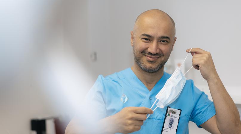 En man i vårdkläder håller ett munskydd framför ansiktet.