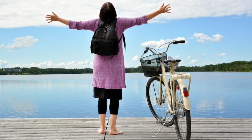 Kvinna på brygga blickar ut mot sjön med händerna utsträckta åt sidorna.