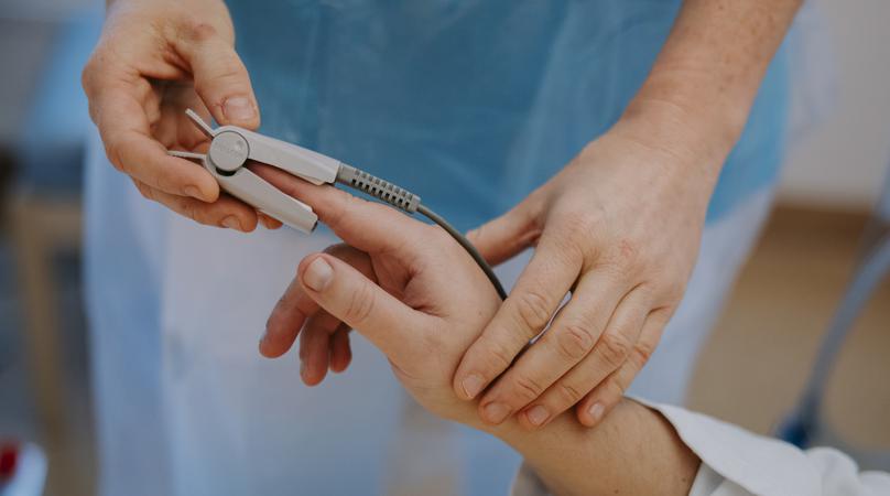 Bilden visar en medarbetares händer som fäster en klämma på en patients pekfinger.
