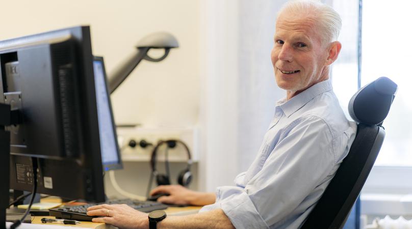 En man sitter i kontorsstol, vid flera skärmar. 