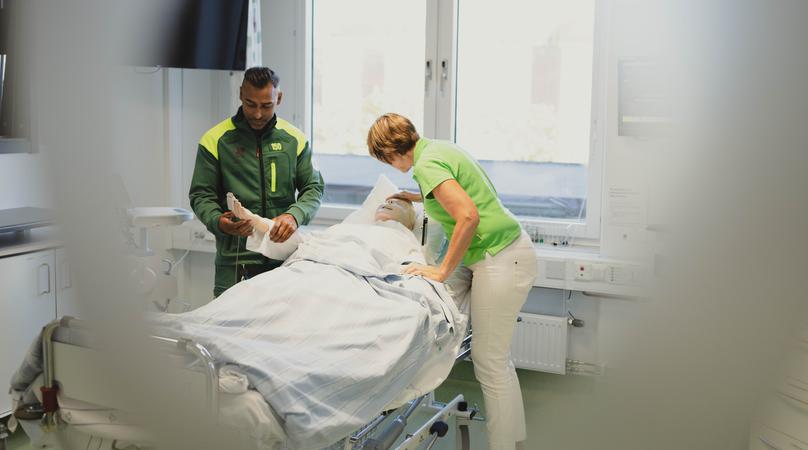 Personal undersöker patient i sjukhussäng.