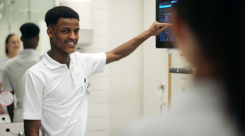 Man i vårdkläder pekar på en skärm.