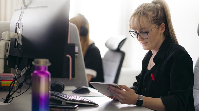 En kvinna sitter vid ett skrivbord och jobbar med en surfplatta.
