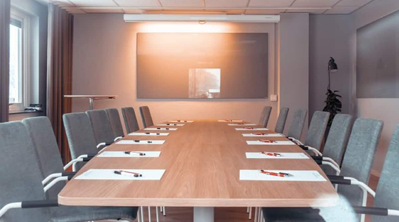 Konferensrum med ett långt avlång bord, flertalet stolar och en projektor.