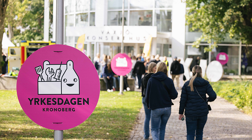 Elever går mot konserthuset bredvid en rund, rosa skylt med texten Yrkesdagen Kronoberg.