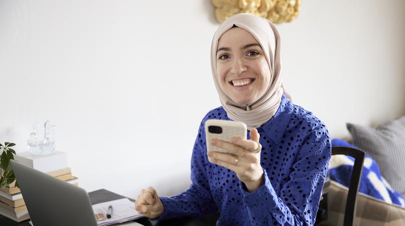 Tjej med hijab sitter vid dator och mobil