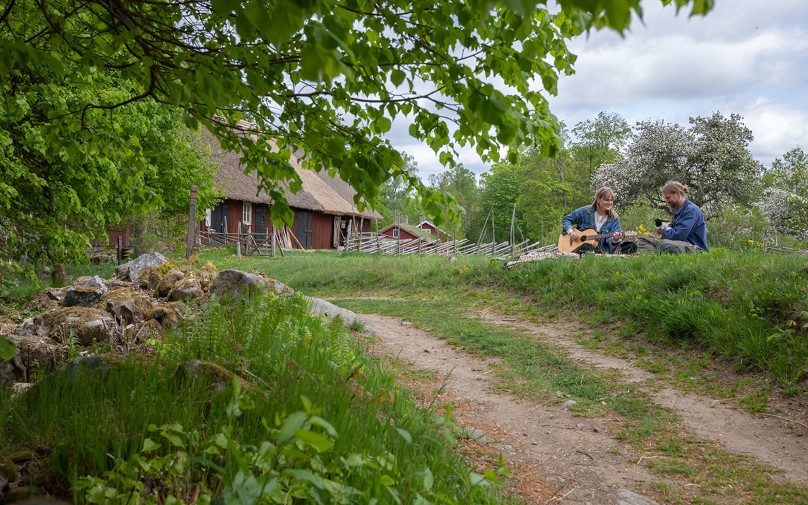 Två personer sitter i gräset på en gård och spelar gitarr och sjunger.