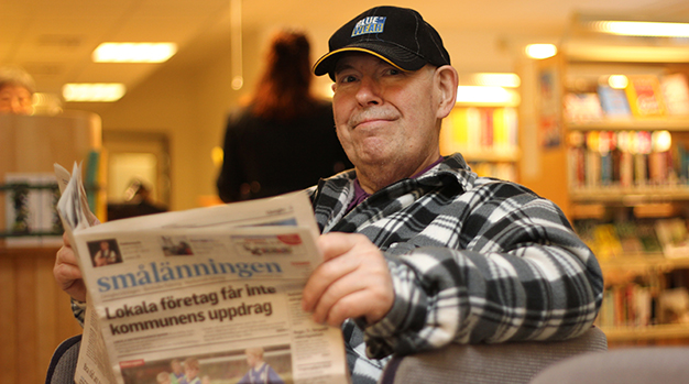 En man i keps sitter och läser en dagstidning.